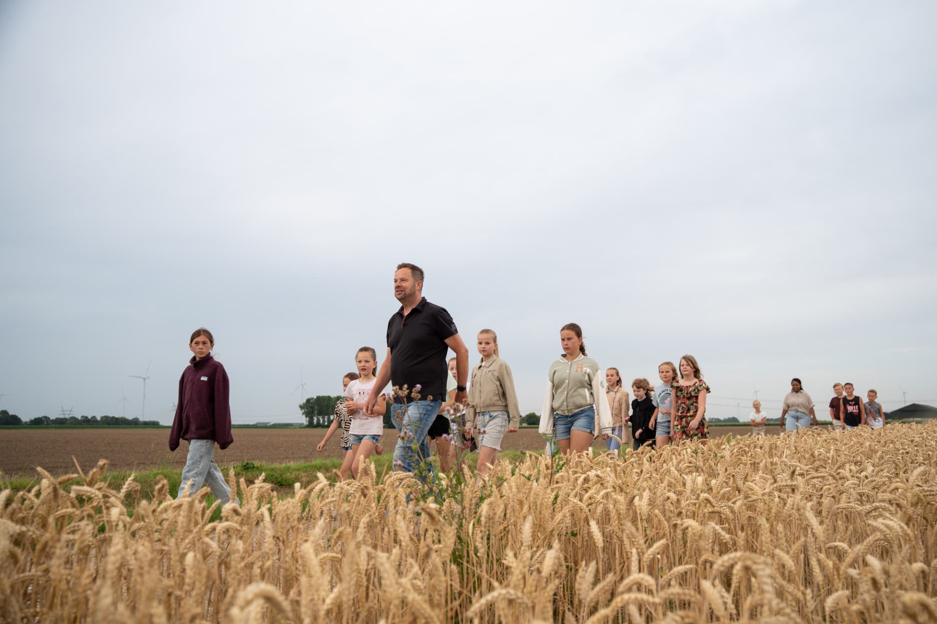 De boer loopt met leerlingen door het graanveld